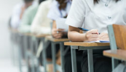 Students Taking Exam in Classroom Setting. Students in uniforms are seated in a classroom, writing answers during an exam, highlighting focus and academic testing. Past papers